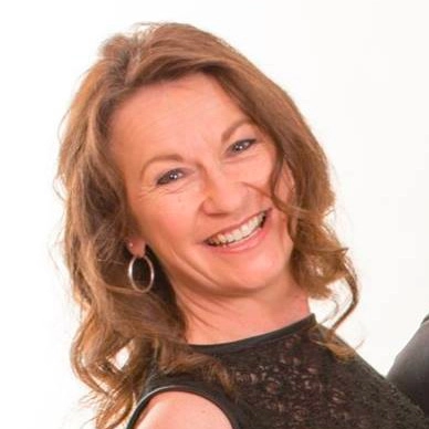 A cheerful woman with curly brown hair and hoop earrings in a black lace top.