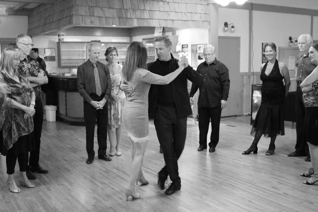 A black-and-white photo of a couple dancing in a room with onlookers.