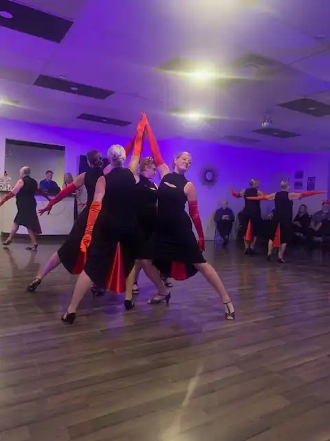 Group of dancers performing in black and red outfits, forming a synchronized pose under purple lighting at a 2025 dance event.