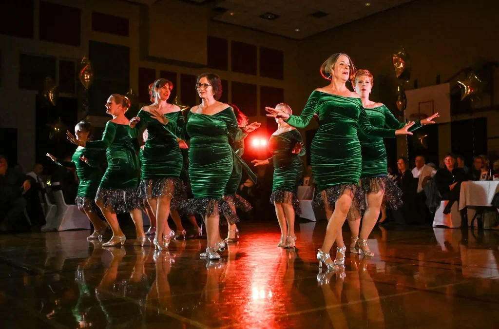 A group of women in green dresses performing a synchronized dance on a polished floor.