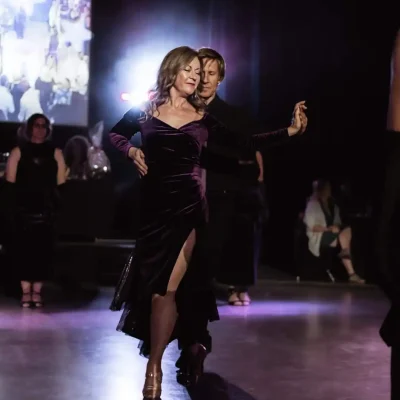A couple dancing gracefully on stage under dramatic purple lighting
